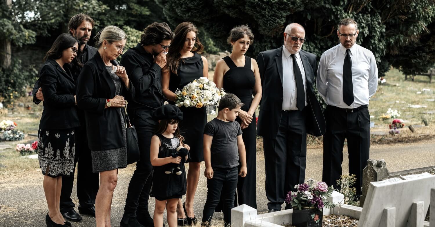 Familie in Trauerkleidung nimmt Abschied am Grab auf dem Friedhof