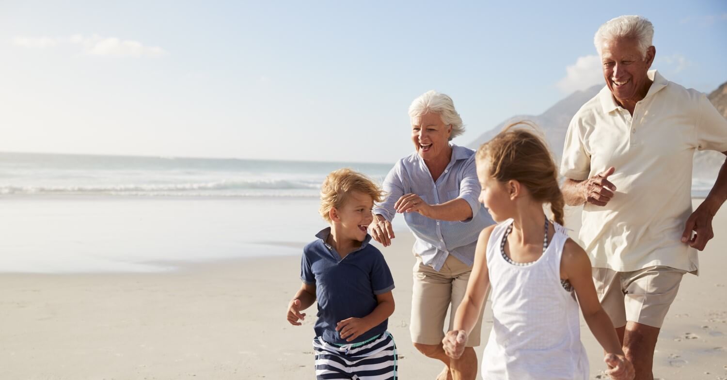 Großeltern laufen mit ihren Enkelkindern, einem Jungen und einem Mädchen, am Strand entlang