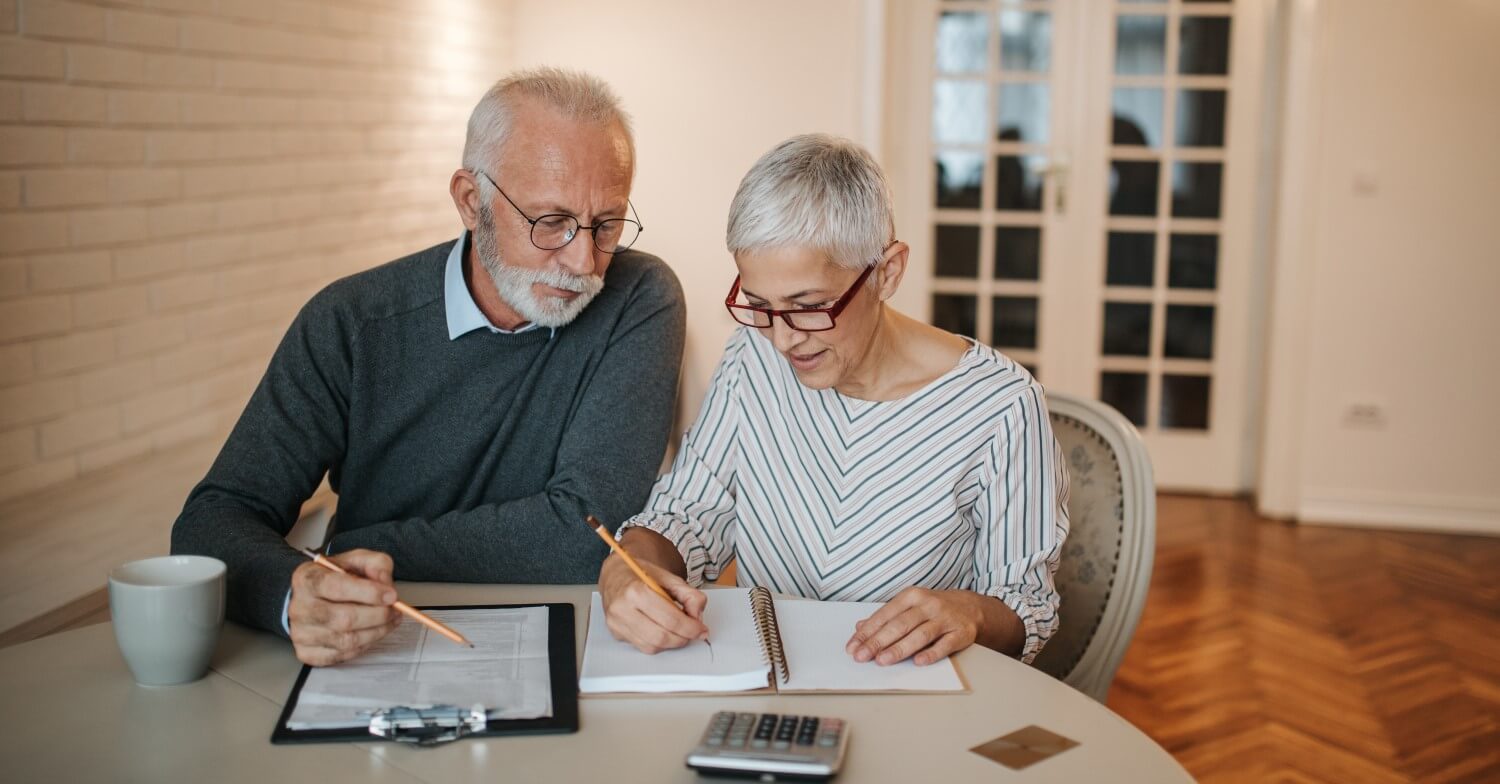 Ein Rentnerpaar sitzt am Wohnzimmertisch und führt Berechnungen durch