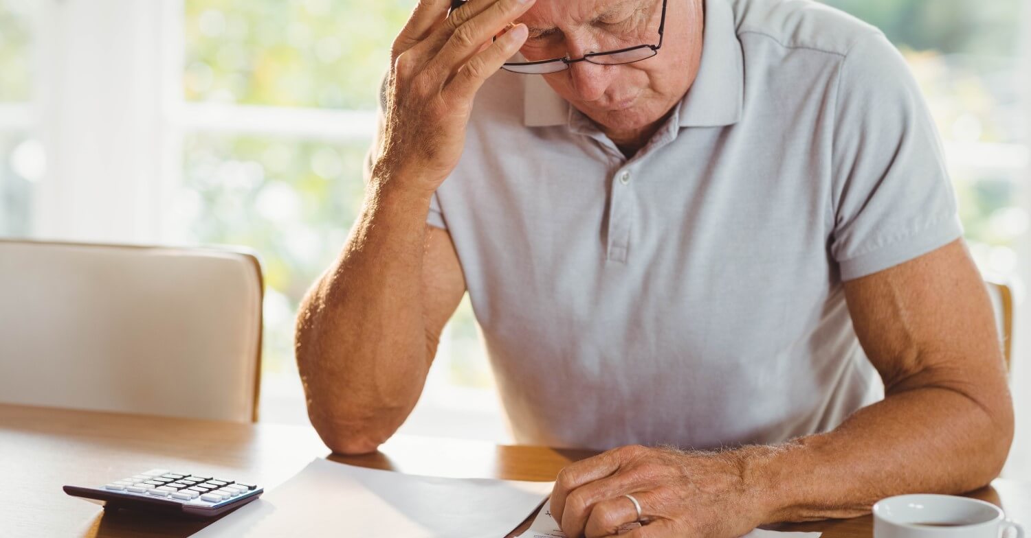 Ein Rentner sitzt am Tisch, hat seinen Kopf in die Hand gestützt und füllt seine Steuererklärung aus