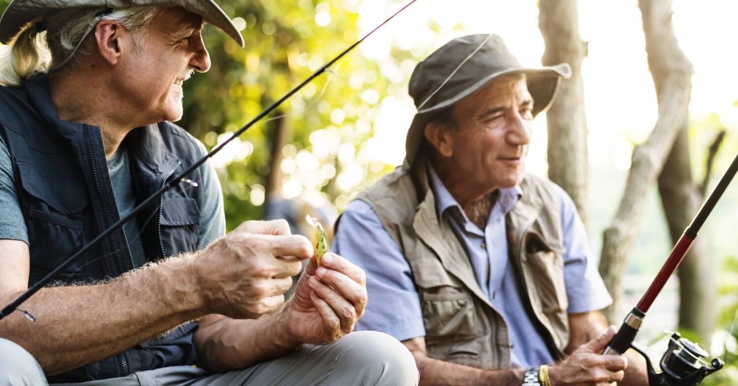 Zwei Rentner angeln, beide Tragen Westen und Hüte, sie halten Angeln in den Händen