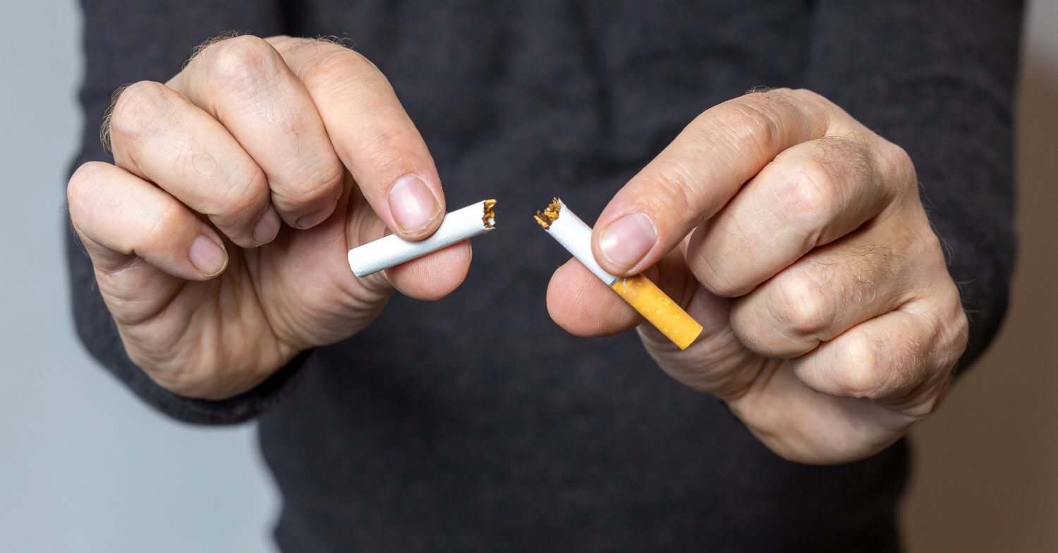 Ein Mann hält seine Händer vor sich gestreckt, in denen er eine in der Mitte durchgebrochene Zigarette hält