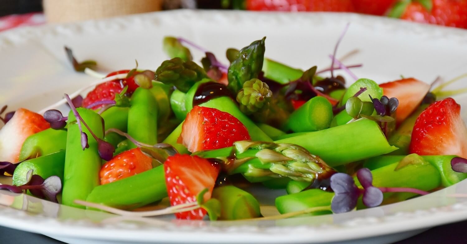 Ein Teller mit einem bunten Salat aus grünem Spargel und Erdbeeren