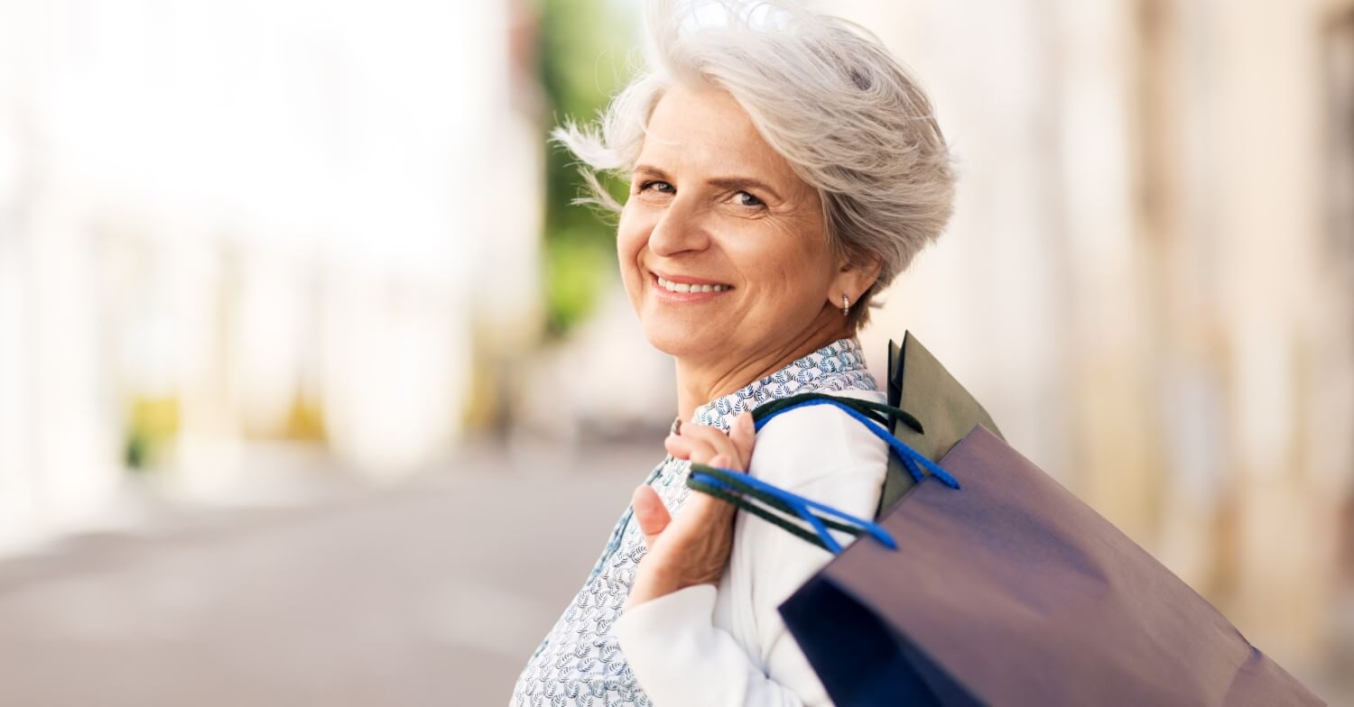 Eine Rentnerin mit grauen Haaren trägt eine Einkaufstasche über der Schulter