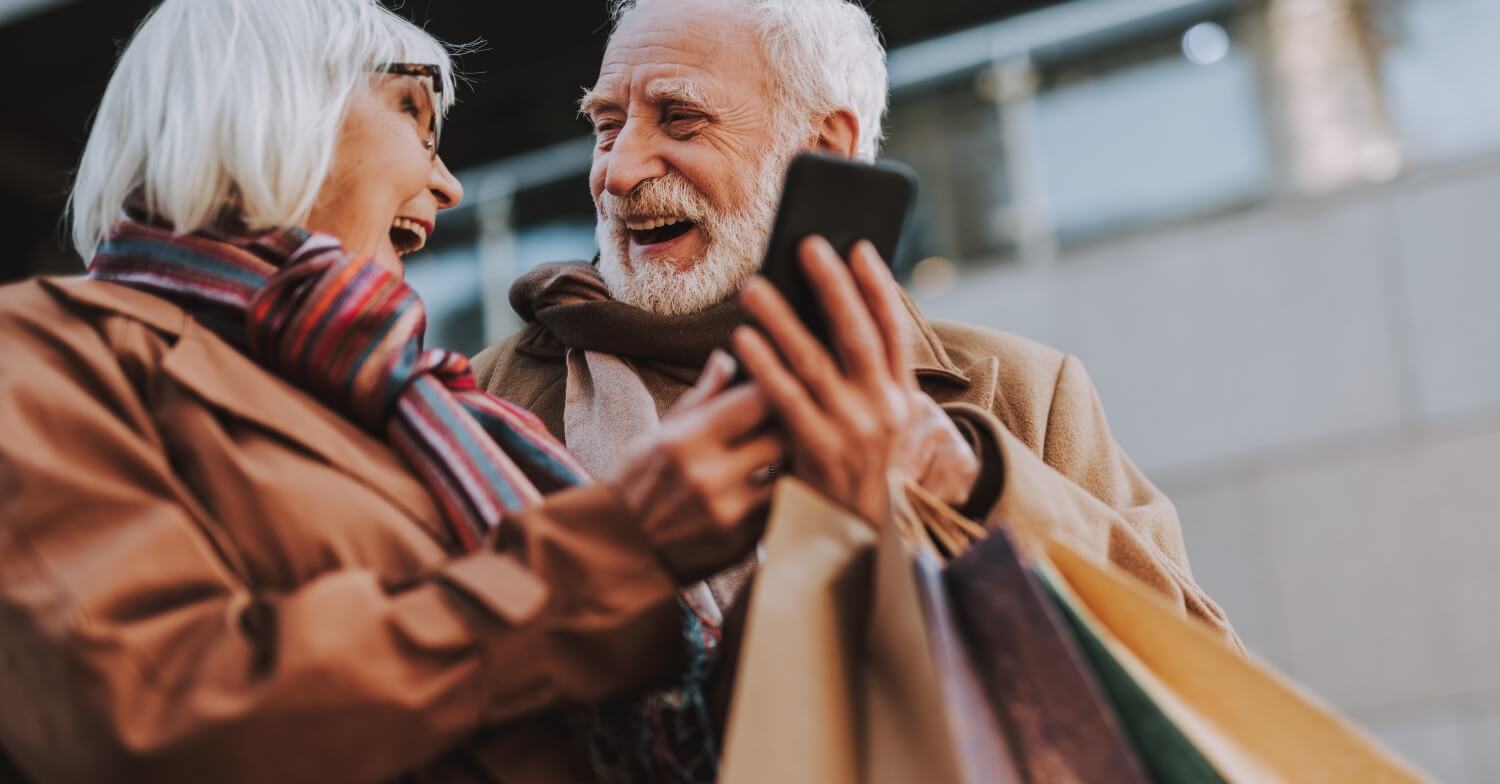 Ein lachendes Rentnerpaar trägt zahlreiche Einkaufstaschen vom Stadtbummel