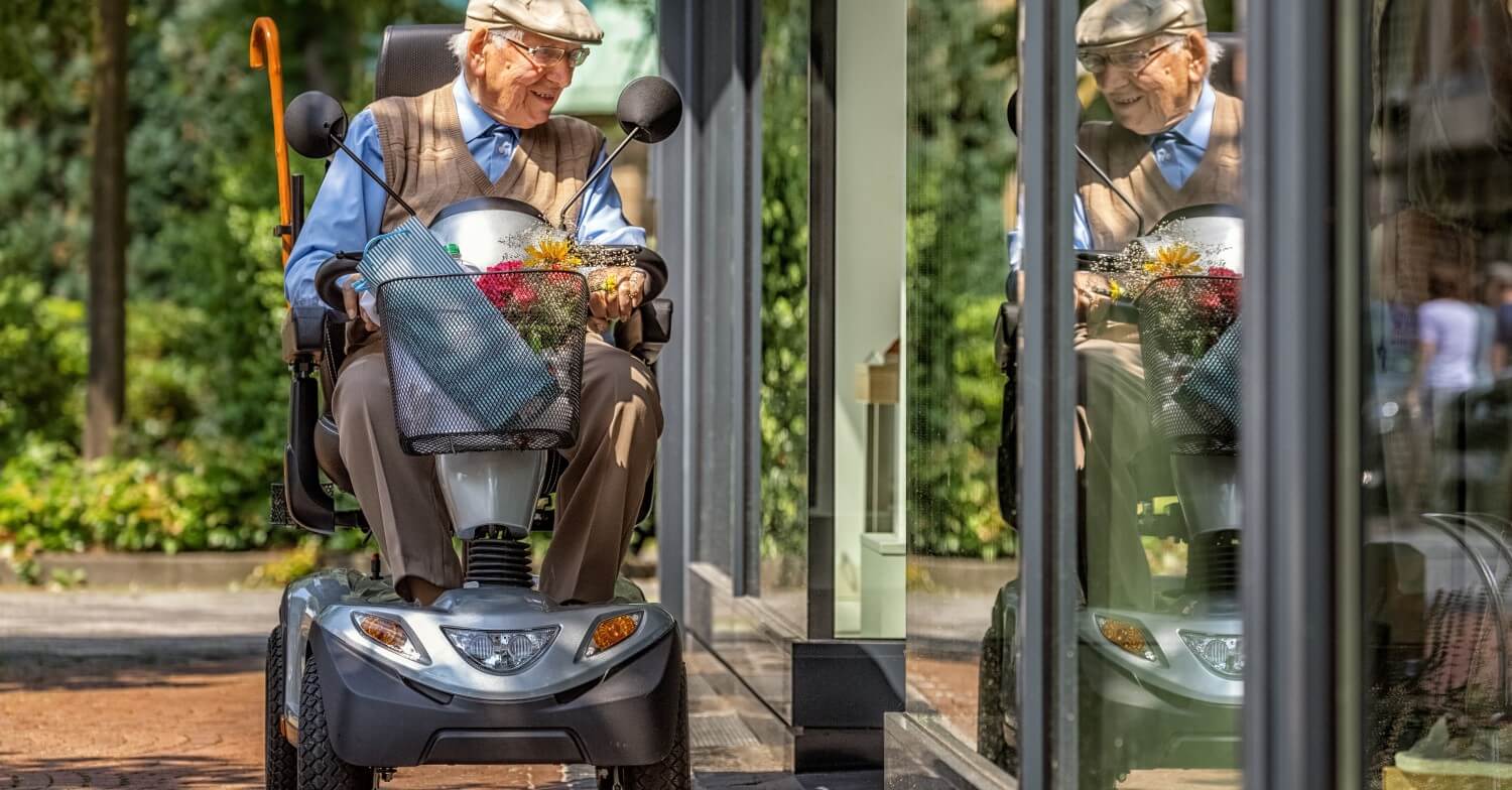 Ein Rentner fährt auf einem E-Mobil / Scooter an einem Schaufenster vorbei